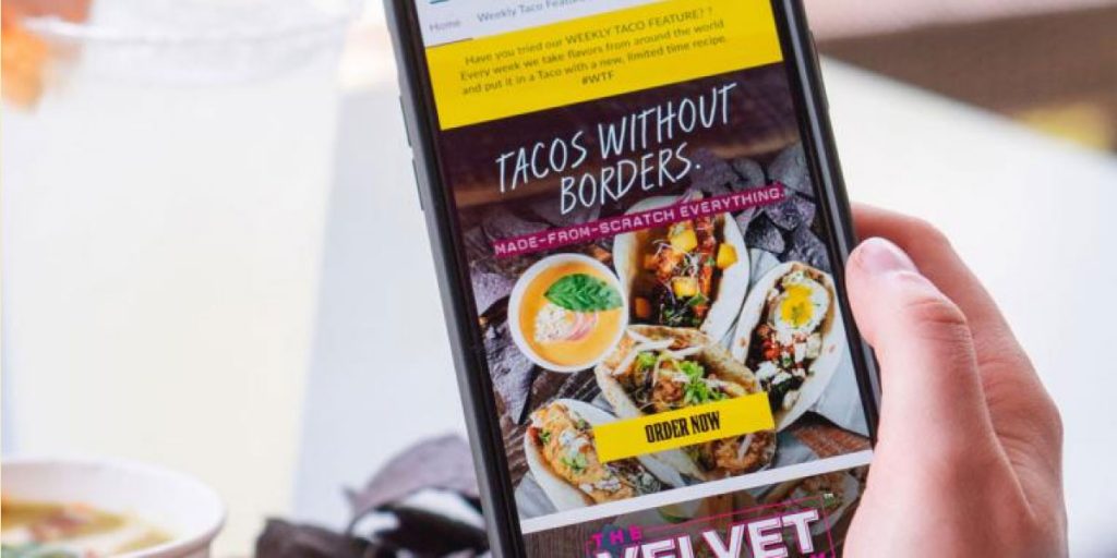 Photo of a person's hand holding a phone with the Velvet Taco mobile app highlighting giveaway